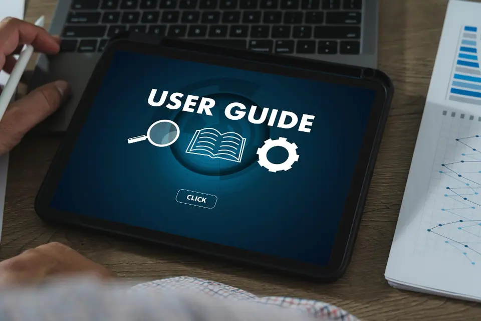 A tablet on a desk displays a screen titled "USER GUIDE" with icons for search, book, and settings—ideal for learning about moisture mitigation or dehumidification services. A hand holding a pen is poised nearby, ready to take notes.