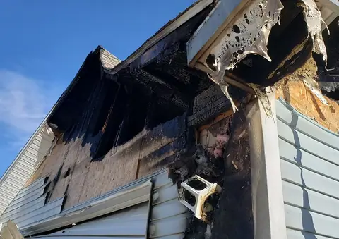 Siding and roof of a house severely damaged by fire, with blackened wood, melted materials, and exposed insulation visible under clear blue sky—highlighting hidden dangers after a fire that can compromise safety.