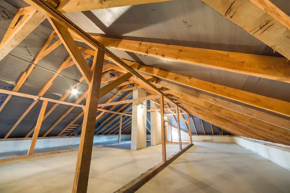 A spacious, unfinished attic with exposed wooden beams, slanted ceiling, concrete floor, and a few light fixtures—ideal for those considering moisture mitigation or drying and dehumidification to protect the space.
