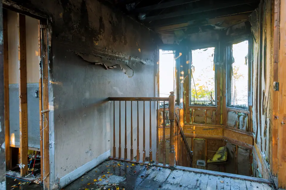 Interior of a house with severe fire damage; walls and ceiling are blackened and charred, with exposed beams and debris scattered on the floor—possible damage worsened by a burst pipe in Winnsboro, TX.