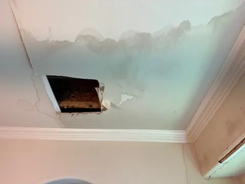 Water-stained ceiling with a square access hole cut to reach the leak