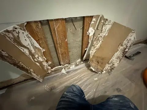 Wet drywall cut open to the studs after water damage, plastic laid over the floor