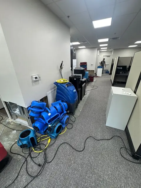 Air movers lined up along an office hallway with the wall base opened