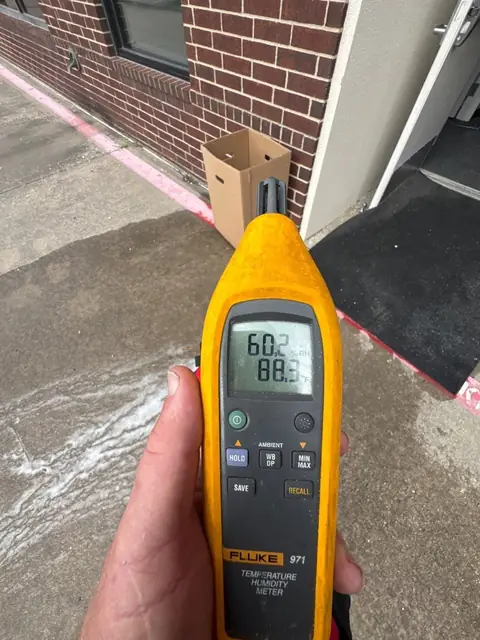 Hand-held hygrometer showing temperature and humidity at a wet entrance