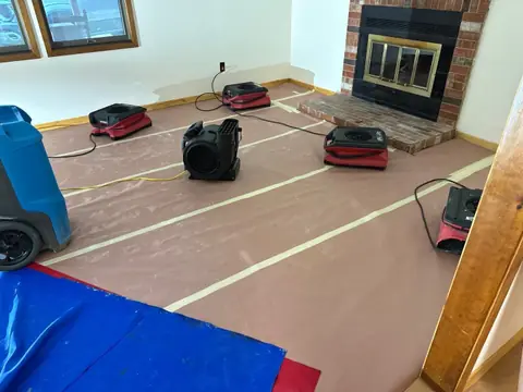 Air movers and a dehumidifier on protected flooring in a living room