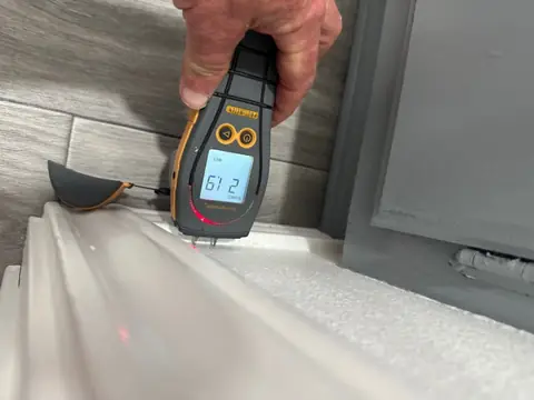 Pin moisture meter testing a baseboard beside a vanity