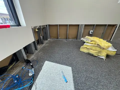 Office wall cut open along the bottom with wet insulation bagged on the carpet