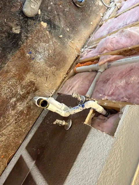 Plumbing exposed where a floor and wall were opened, insulation beside it