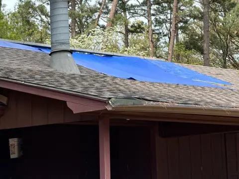 Blue tarp fastened over a damaged section of shingle roof