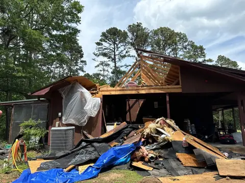 House with a collapsed roof section and debris piled in the yard after a storm