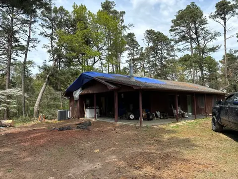 House with a blue tarp over storm-damaged roof sections among pine trees
