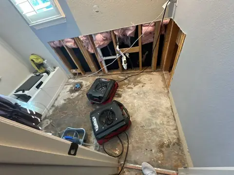 Upstairs room with drywall cut away at the bottom and two air movers drying the wall