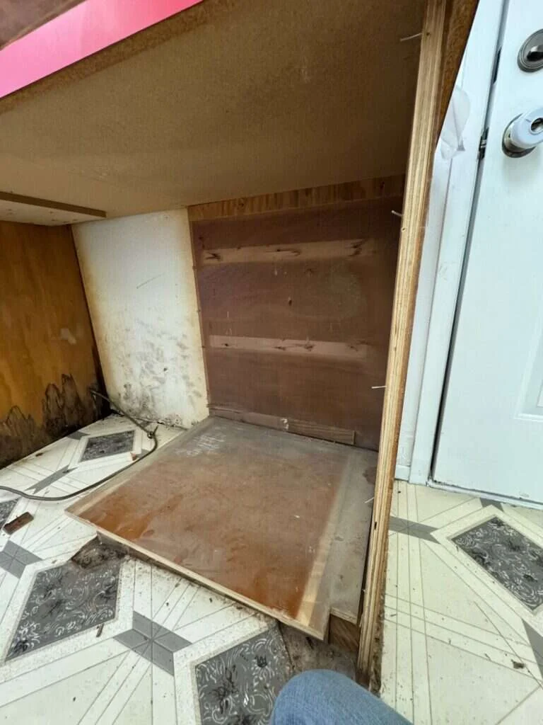 Kitchen cabinet bottom board removed during water damage inspection, exposing moisture staining and mold on the wall and cabinet framing from a slow dishwasher leak